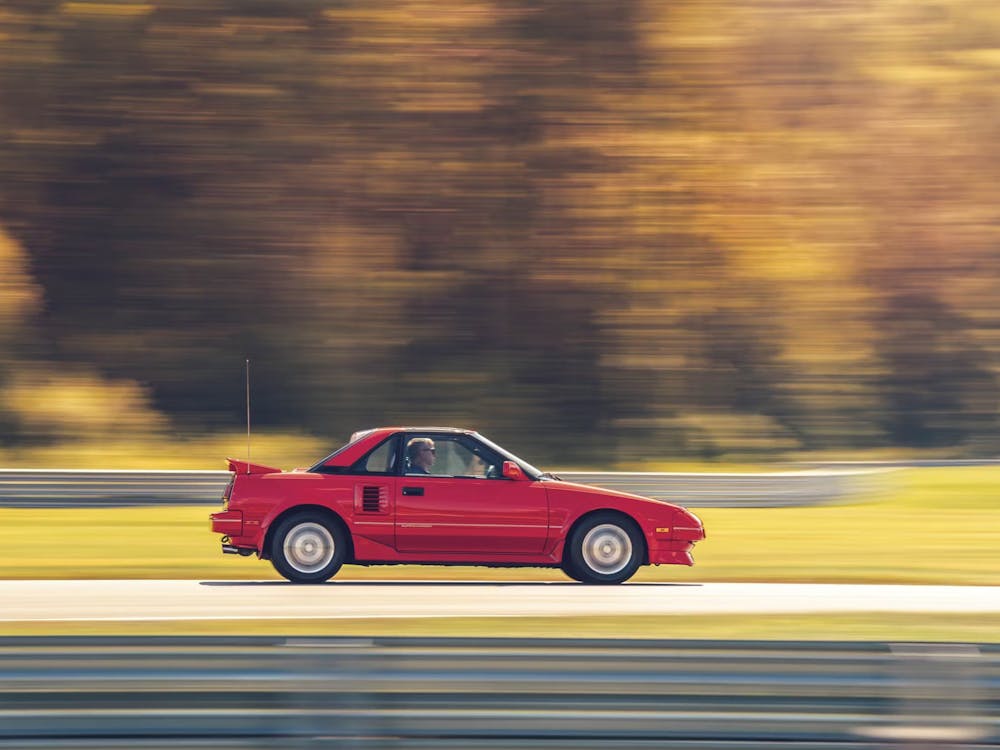 A red Toyota MR2 driving fast on a sunny autumn day