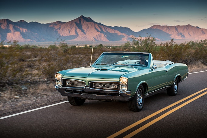 Classic green Pontiac GTO driving away from mountain sunset, three quarter view