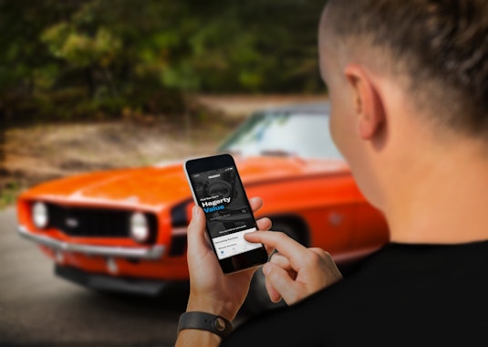 man using Hagerty Valuation App on iphone in front of red classic car