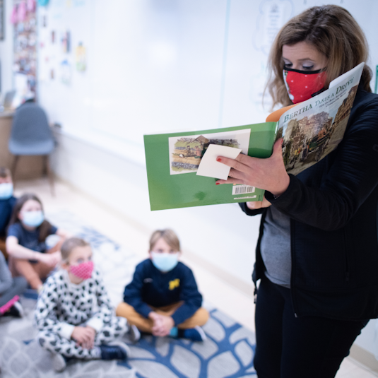 A woman reads a book to an elementary school class.