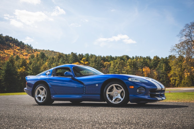 A blue Dodge Viper parked in front of an autumn-colored forest.