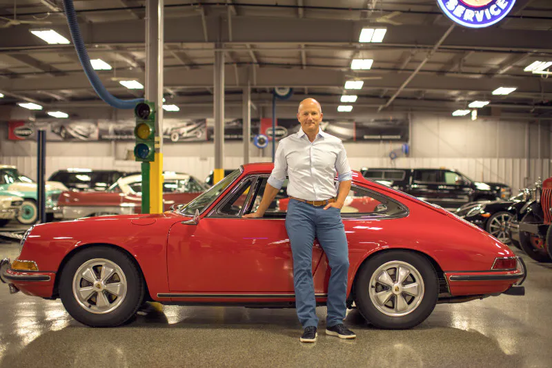 McKeel Hagerty stands next to a red Porsche in the Hagerty Garage