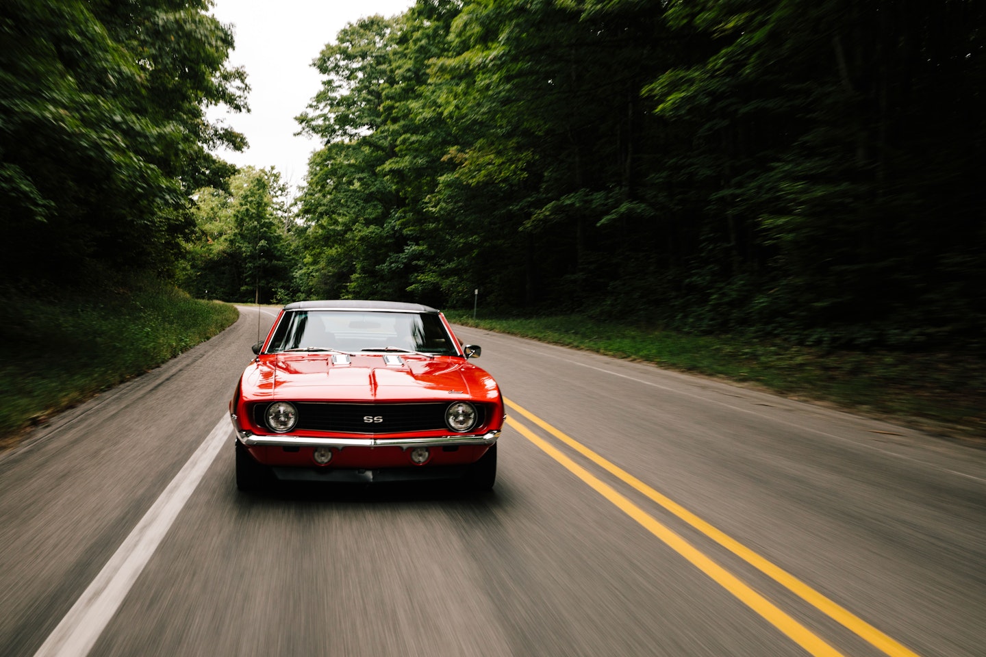 A red vintage Camero driving on a road through the woods