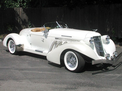 A replica of a white 2003 Auburn Speedster, parked in front of a fence.
