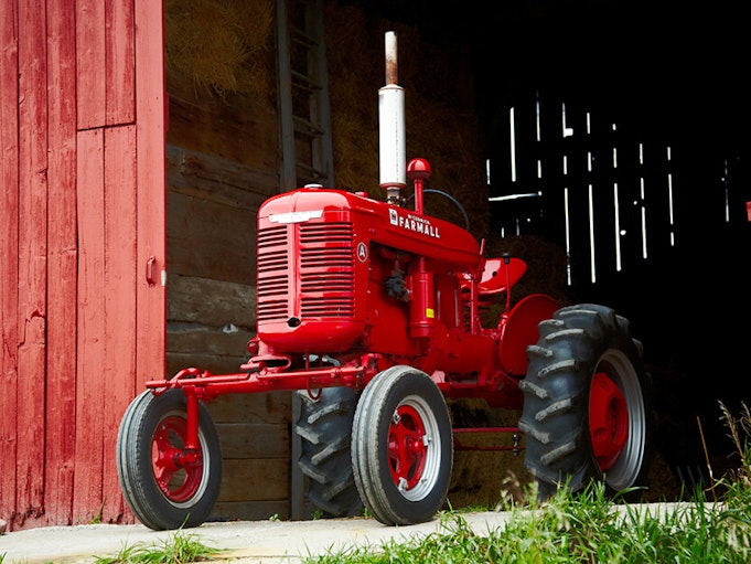 A red collector tractor in front of a red barn.