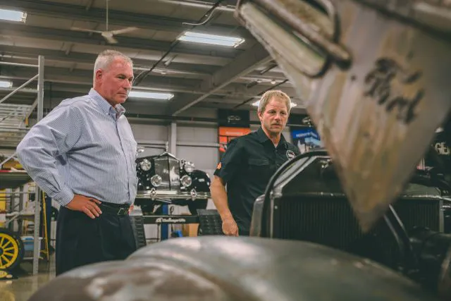 A Hagerty employee standing next to a Learning Garage employee as they inspect the engine of a vintage Ford pickup truck.