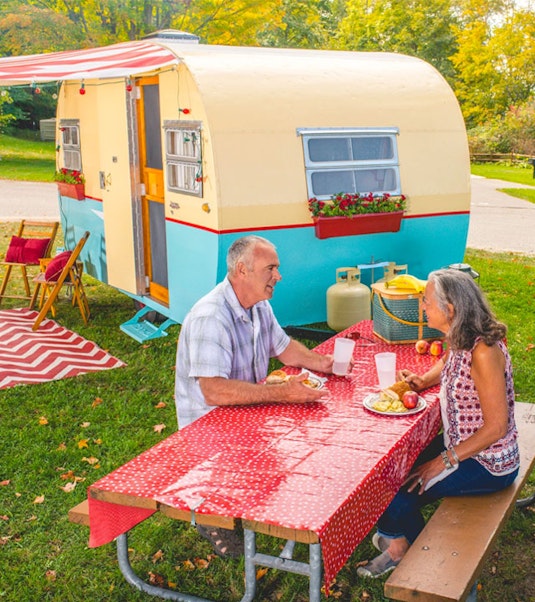 Two people picnicking in front of a vintage camper trailer