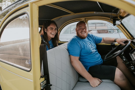 A man and woman are smiling and sitting inside of a yellow collector vehicle
