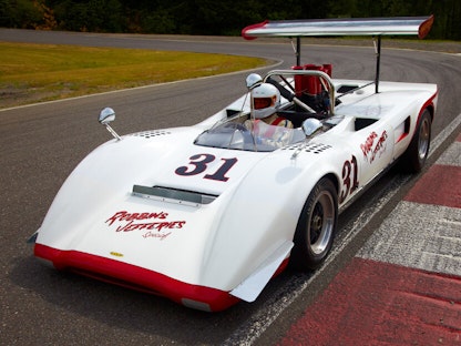 A driver sitting in a parked white collector race car.