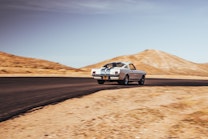 A white Shelby Cobra drives down a secluded road in the desert.