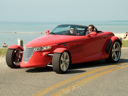 A couple enjoying a cruise in a red classic car by a beach.