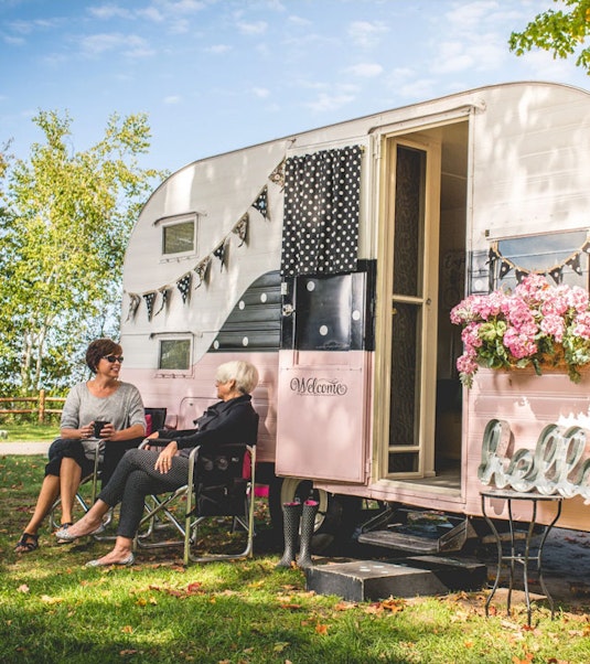 Two people sitting in front of a vintage camper trailer