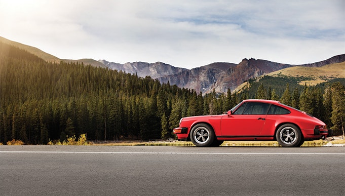 Red Porsche 911 parked on road, mountains in background