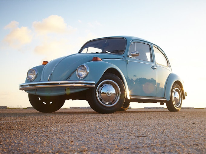 A sky blue collector Volkswagen Beetle parked on concrete with blue sky in the background.