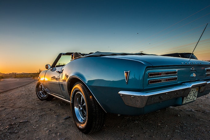 Back three-quarter view of classic Pontiac Firebird convertible directed at the sunset in background