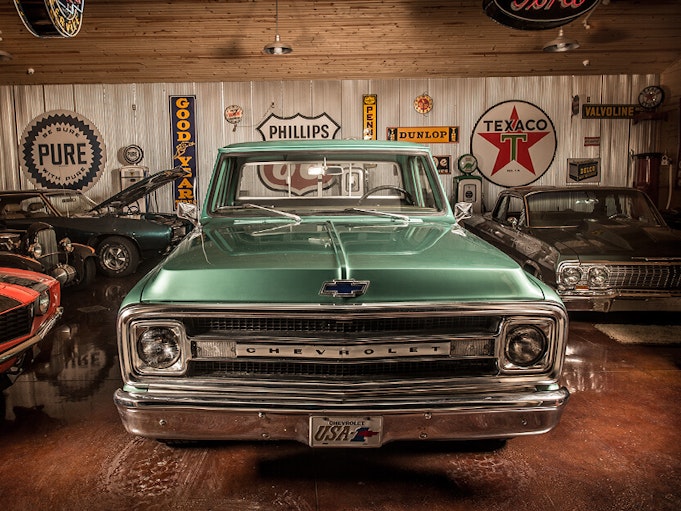 A green collectible car parked in a garage with other collectible vehicles and vintage signs.
