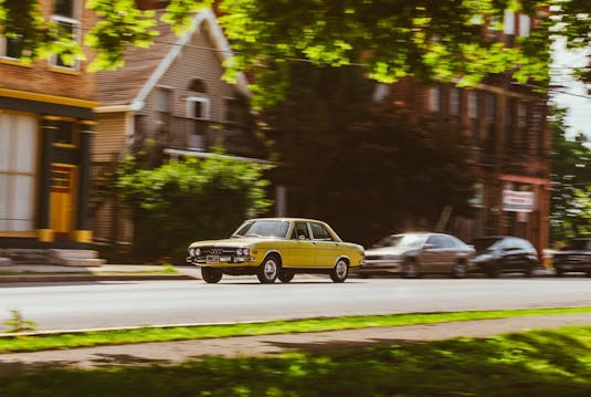 Yellow car driving down residential street.