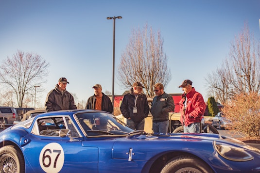 group of five men standing outside looking at a vintage race car
