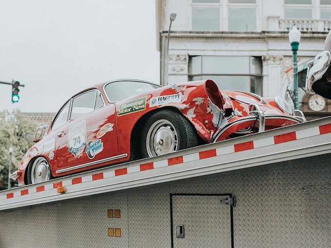 A red Porsche with a broken headlight and dented frame, being pulled up a trailer.