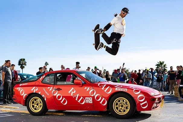 A skateboarder jumping over a red classic car with Radwood written all over the vehicle