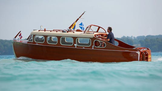 A man directing a collector boat through teal water, with woods in the background.