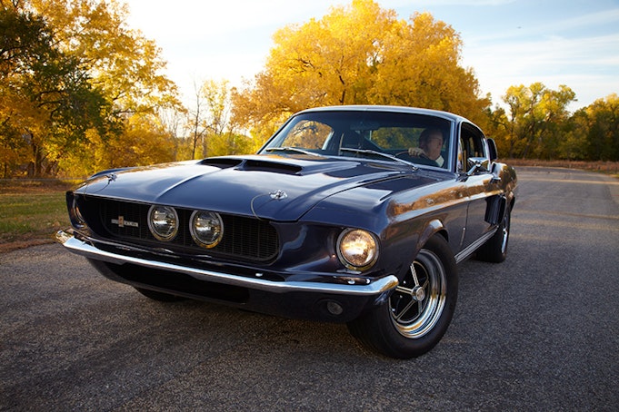 Black classic Mustang driving straight towards the camera with sunset in background