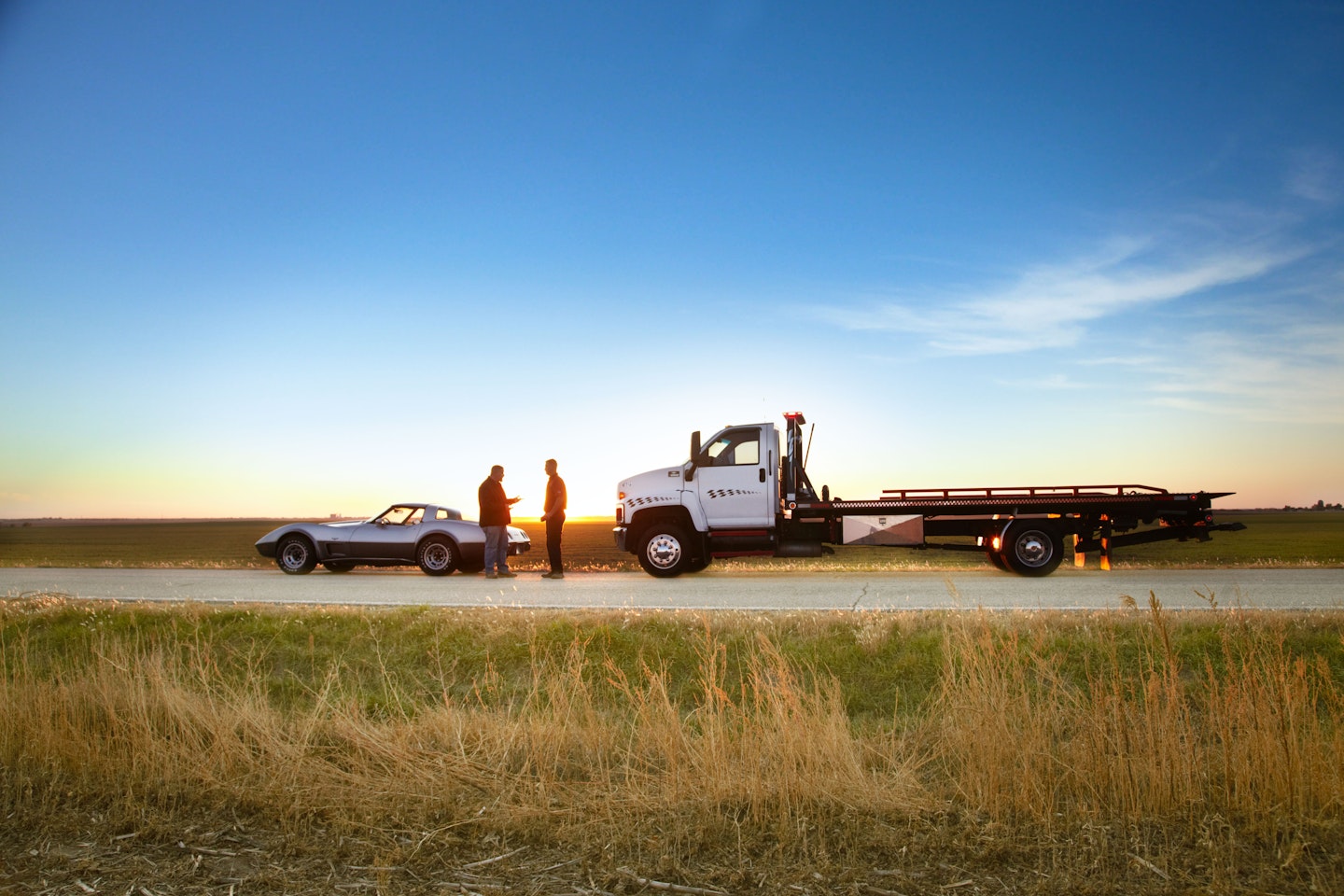 classic car being towed on rural road at dusk