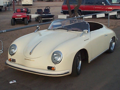 A replica of a cream 1955 Porsche Speedster, with other vehicles in the background.