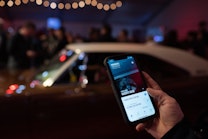 Hand holding phone showing Hagerty Valuation Tools app in foreground, car in background