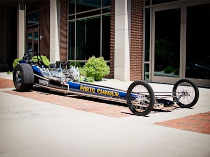 A long blue collector race car parked in front of a building.