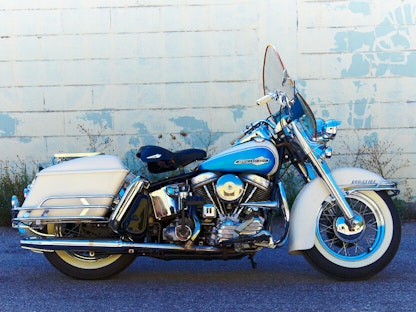 A white collector motorcycle parked in front of a whitewashed brick wall.