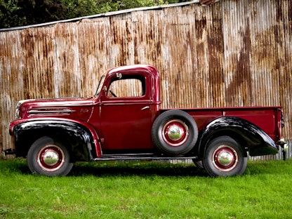 A red collector pickup truck parked on grass in front of a wooden fence.